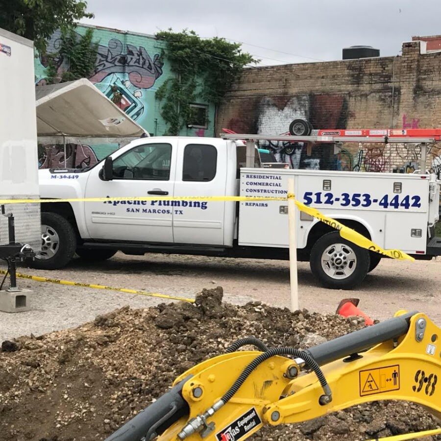 Apache Plumbing lettered work truck at a downtown sewer excavation beside a mini-excavator